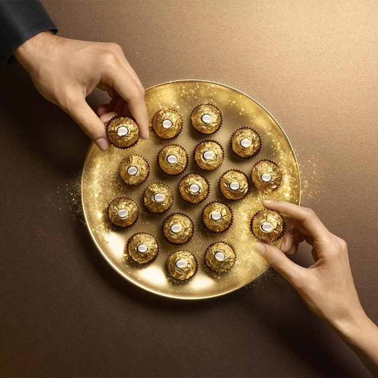 Deux mains prennent des Ferrero Rocher sur un plateau scintillant.
