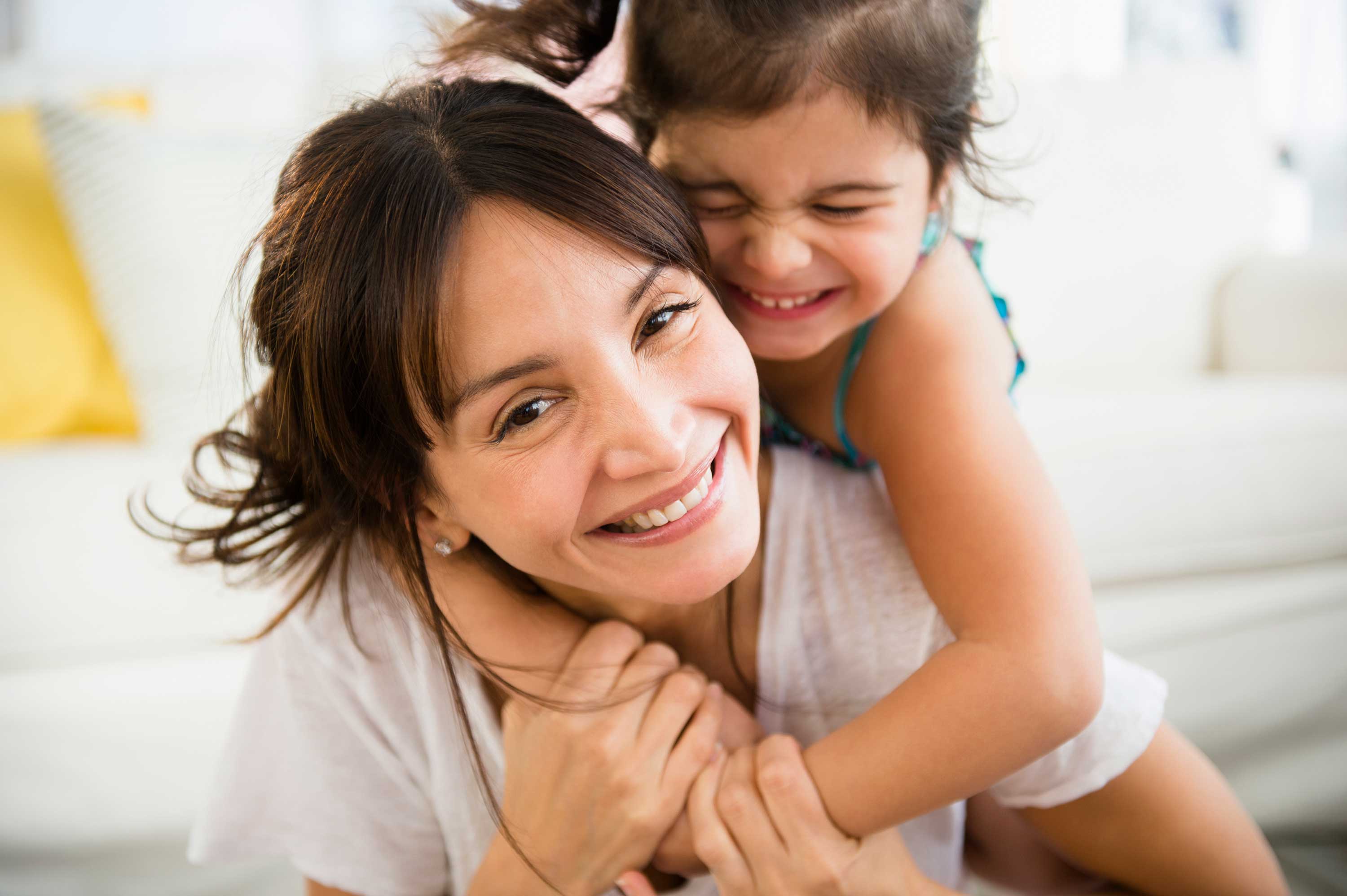 Deux personnes souriantes, une famme e une petite fille l'une étreignant l'autre par derrière avec affection.