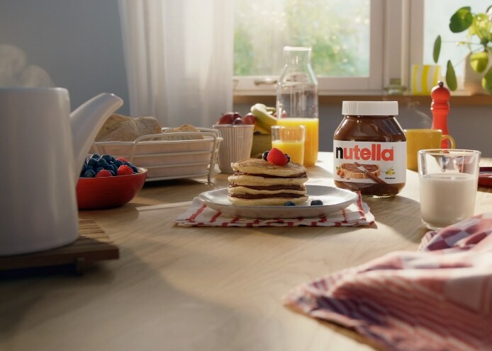 Petit-déjeuner sur table avec pancakes garnis de Nutella et fruits, jus d'orange et lait.