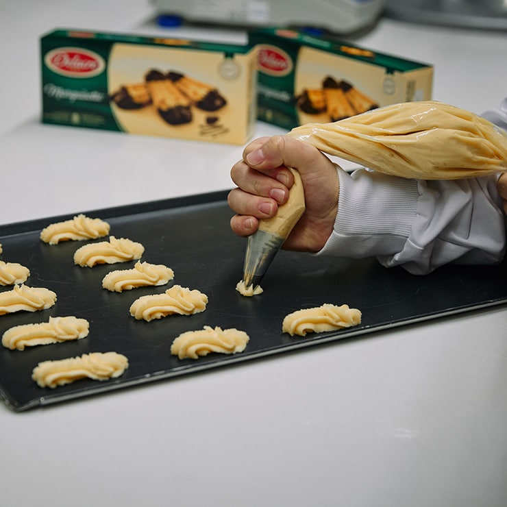Personne utilisant une poche à douille pour préparer des biscuits sur une plaque de cuisson avec a Delacre paquet 