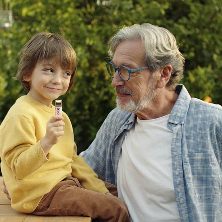 Un enfant et un homme sourient ensemble, l'enfant tenant une barre Kinder.