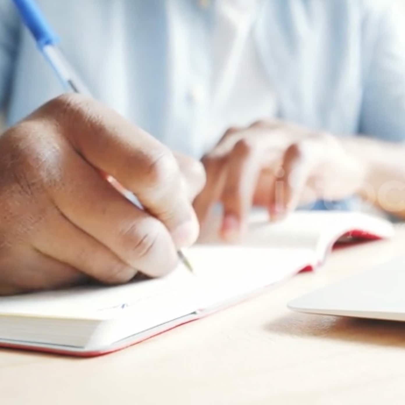 Un homme concentré en train d'écrire dans un cahier, assis à un bureau.