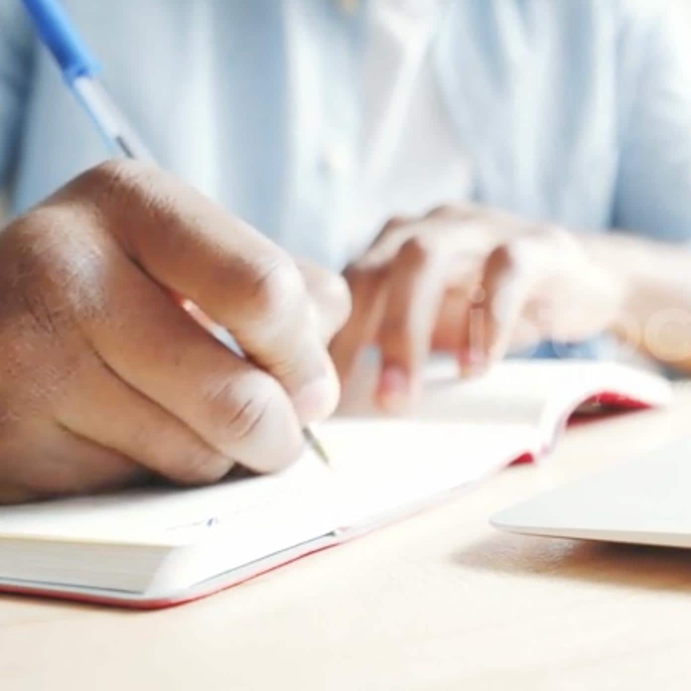 Un homme concentré en train d'écrire dans un cahier, assis à un bureau.
